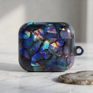 May include: A protective case for wireless earbuds featuring a dark, iridescent mosaic pattern that mimics crushed opal. The surface displays deep blues, purples, and flashes of orange and green light across a fragmented, geometric tile design.