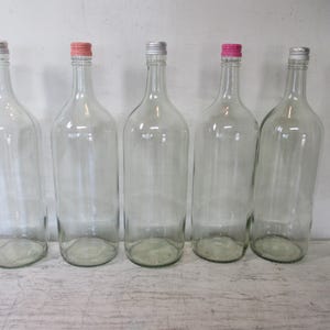 May include: Five clear glass bottles arranged in a row, each featuring a tall, cylindrical body and a narrow neck. Three bottles have silver-colored metal caps, while two bottles are topped with distinct pink-colored metal caps.