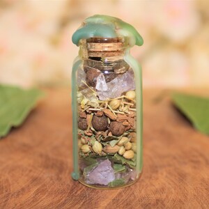 May include: A small glass bottle with a green wax seal on the top. The bottle is filled with various herbs, spices, and crystals.