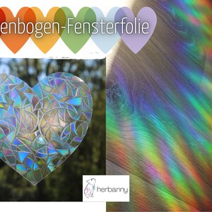 Puede incluir: Un film para ventanas de arcoíris en forma de corazón, con un efecto de arcoíris en el suelo de madera detrás. El texto "Regenbogen-Fensterfolie" está en la parte superior de la imagen.
