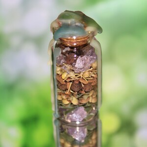 May include: A small glass jar with a cork top is filled with various herbs, spices, and crystals. The jar is sealed with a layer of melted wax, giving it a rustic and magical appearance.