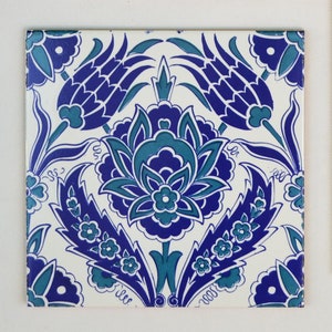 Könnte beinhalten: Quadratische Keramikfliese mit einem floralen Muster in Blau- und Türkistönen auf weißem Hintergrund. Das Muster zeigt stilisierte Blumen und Blätter, die ein symmetrisches und dekoratives Motiv bilden. Die Fliese ist für die Inneneinrichtung oder als dekoratives Element geeignet, ca. 20 cm x 20 cm.