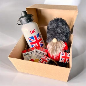 Puede incluir: Caja de regalo con temática británica que contiene una botella de agua blanca con la bandera del Reino Unido, un gnomo con abrigo rojo y sombrero negro y galletas de mantequilla. La caja es de cartón.
