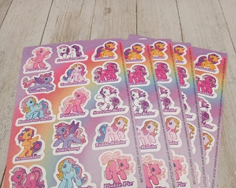 May include: A set of eight sheets of stickers featuring My Little Pony characters. Each sheet has a rainbow background and features a different pony with its name printed below. The ponies are pink, purple, blue, yellow, and orange.