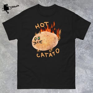 Może przedstawiać: Czarny T-shirt z kreskówkowym obrazkiem ziemniaka w kształcie kota z płomieniami wychodzącymi z jego pleców. Na koszulce nadrukowany jest napis "HOT CATATO".