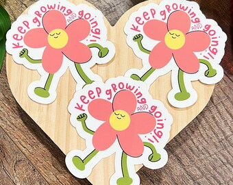 Peut inclure: Trois autocollants de fleurs roses avec des tiges vertes et des visages souriants. Chaque autocollant porte le texte "Keep growing and going!" dans un cercle blanc autour de la fleur.