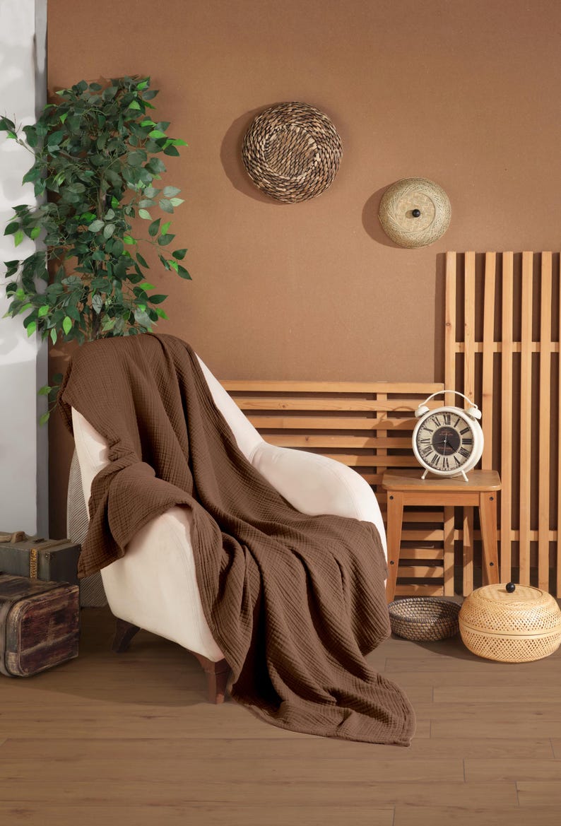 May include: A solid dark brown waffle-textured throw blanket draped over a cream-colored armchair. The blanket features a distinct grid-like pattern across its entire surface, with soft folds cascading down the seat and onto the floor.