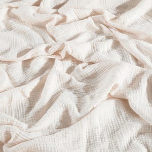 May include: A white cotton muslin fabric with a crinkled texture. The fabric is soft and lightweight, making it ideal for a variety of uses, such as blankets, swaddles, and clothing.