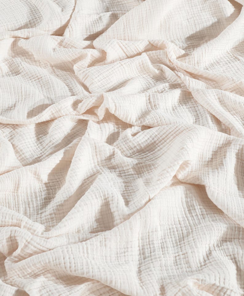 May include: A white cotton muslin fabric with a crinkled texture. The fabric is soft and lightweight, making it ideal for a variety of uses, such as blankets, swaddles, and clothing.