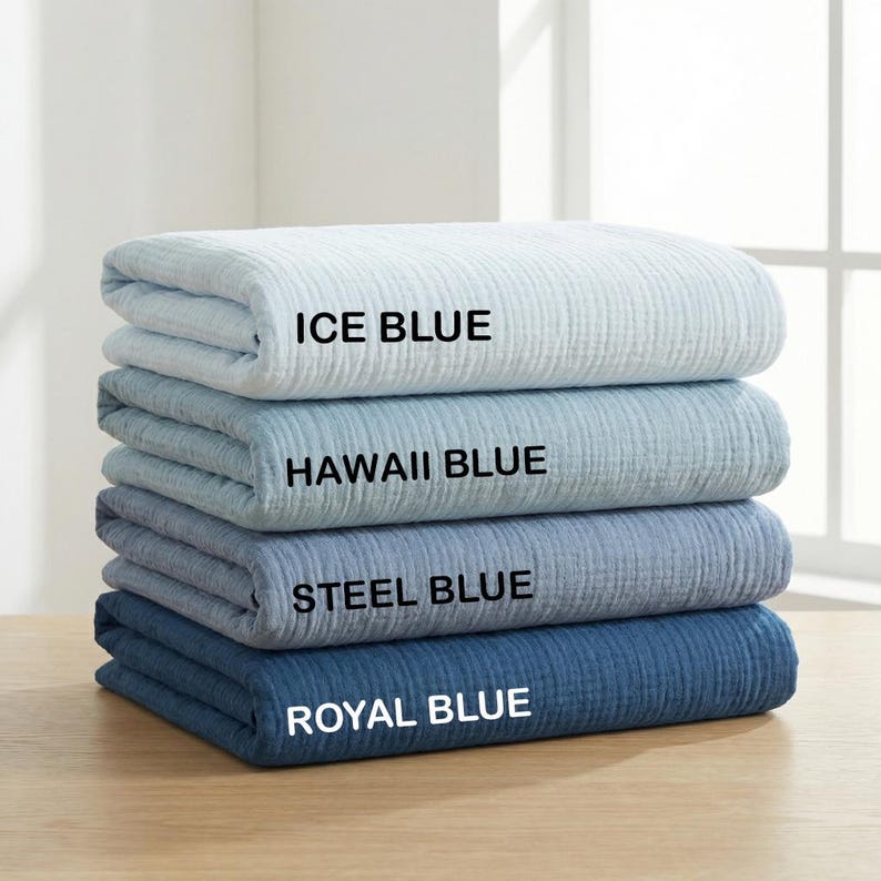 May include: A stack of four folded blankets with a textured, crinkled fabric surface. The blankets are labeled with black text as Ice Blue, Hawaii Blue, Steel Blue, and Royal Blue, showing a gradient of blue shades from light to dark.