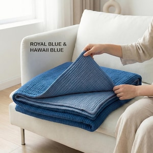 May include: A folded blue blanket with a textured surface is displayed on a white couch. The blanket is a combination of royal blue and Hawaii blue. The text "ROYAL BLUE & HAWAII BLUE" is visible in the image.