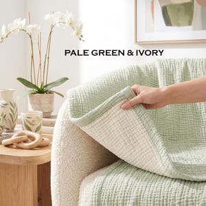 May include: A pale green and ivory blanket with a textured, quilted grid pattern. The blanket is draped over a white, textured armchair. The text PALE GREEN & IVORY is visible above the blanket, which shows a light green top and an ivory underside.