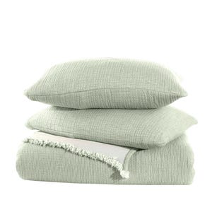 May include: A stack of three sage green waffle weave throw pillows with a matching sage green waffle weave throw blanket. The blanket has a white fringe trim.
