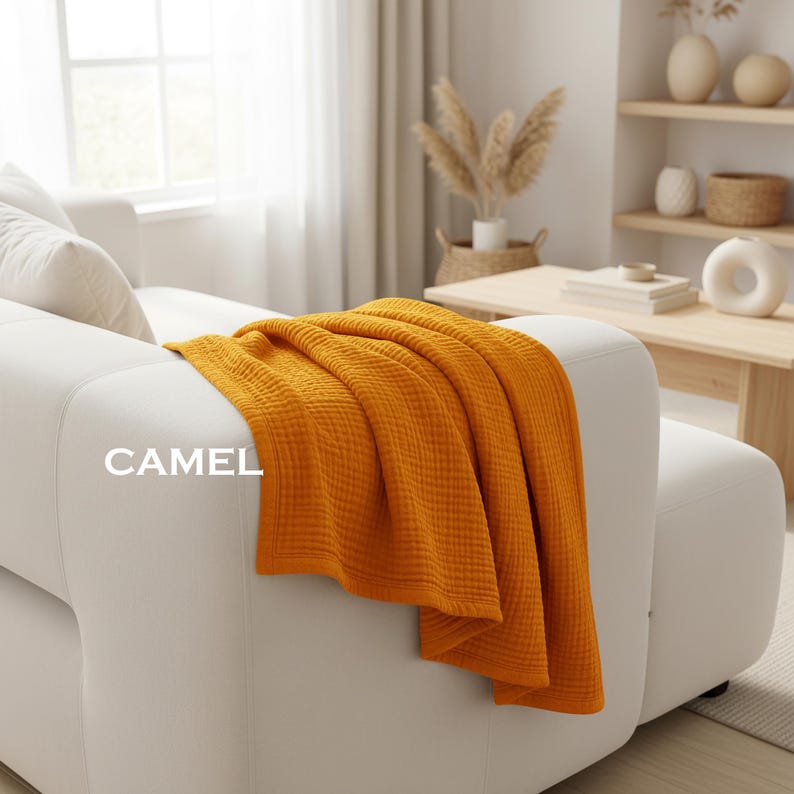 K&ouml;nnte beinhalten: Eine einfarbige, kamelfarbene Wohndecke mit einer strukturierten Waffeloptik, die &uuml;ber die Armlehne eines wei&szlig;en Sofas drapiert ist. Das Wort CAMEL ist in wei&szlig;er Schrift auf der linken Seite der Decke aufgedruckt, die einen ges&auml;umten Rand hat.