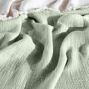 May include: A soft, green, textured throw blanket with a white fringe border.