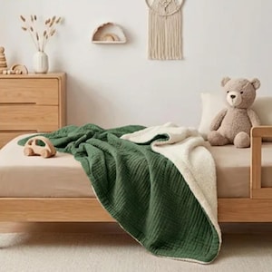 K&ouml;nnte beinhalten: Eine wendbare Decke in Gr&uuml;n und Creme auf einem Holzbett. Ein Holzspielzeugauto und ein Teddyb&auml;r liegen auf dem Bett. Der Raum hat eine neutrale Farbpalette.