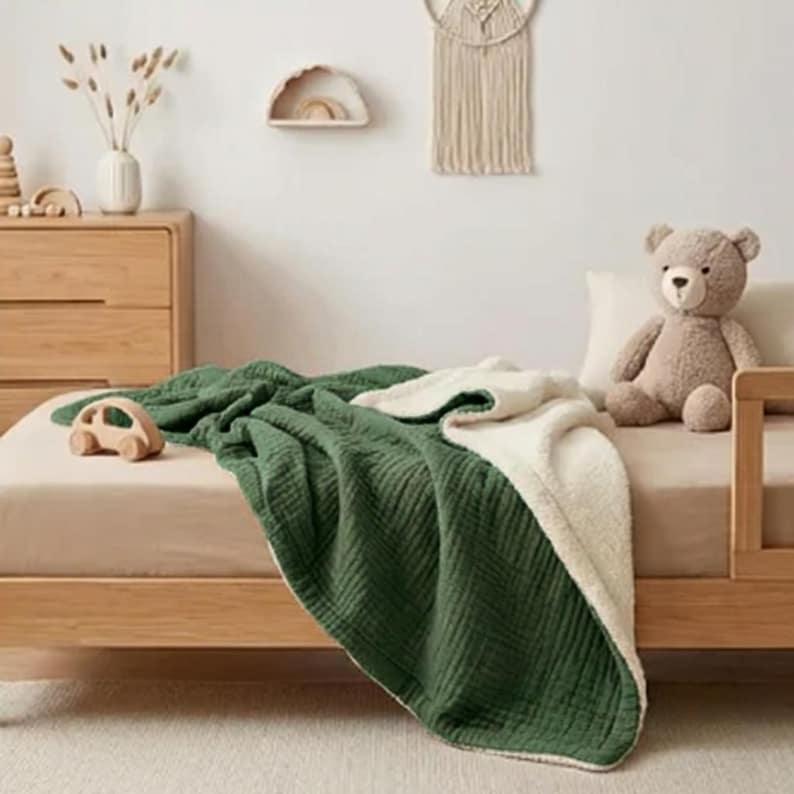 K&ouml;nnte beinhalten: Eine wendbare Decke in Gr&uuml;n und Creme auf einem Holzbett. Ein Holzspielzeugauto und ein Teddyb&auml;r liegen auf dem Bett. Der Raum hat eine neutrale Farbpalette.