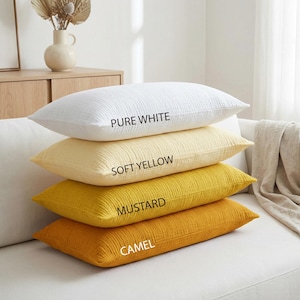 Pode incluir: Quatro almofadas retangulares em tons de branco, amarelo e dourado est&atilde;o empilhadas em um sof&aacute; branco. A almofada superior est&aacute; rotulada como "PURE WHITE", seguida por "SOFT YELLOW", "MUSTARD" e "CAMEL". As almofadas t&ecirc;m uma apar&ecirc;ncia texturizada.