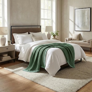 May include: A bedroom scene featuring a bed with white bedding and a green waffle-knit throw blanket. The bed has a wooden headboard and a black metal frame. A beige rug covers the floor. Two lamps and a bench are also visible.