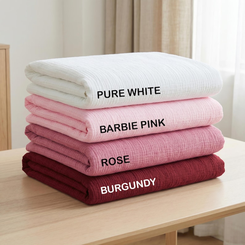K&ouml;nnte beinhalten: Ein Stapel aus vier gefalteten, rechteckigen Decken mit einer strukturierten, geknitterten Stoffoberfl&auml;che. Die Farben von oben nach unten sind als PURE WHITE, BARBIE PINK, ROSE und BURGUNDY beschriftet. Jede Decke liegt ordentlich gestapelt.