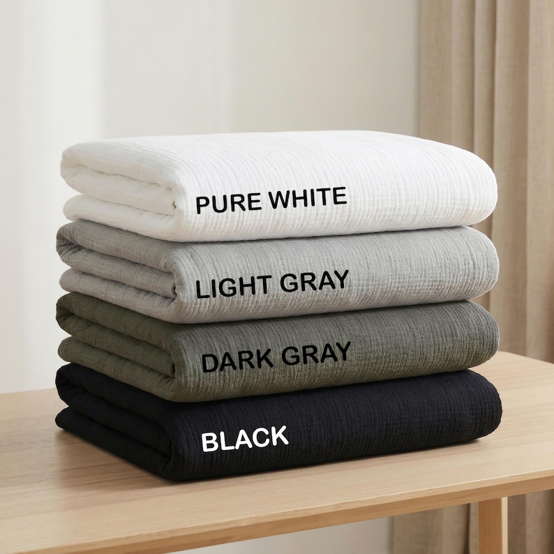 K&ouml;nnte beinhalten: Ein Stapel aus vier gefalteten Decken mit einer strukturierten, geknitterten Stoffoberfl&auml;che. Die Decken sind mit Text beschriftet: PURE WHITE f&uuml;r die oberste, LIGHT GRAY f&uuml;r die zweite, DARK GRAY f&uuml;r die dritte und BLACK f&uuml;r die unterste Decke.
