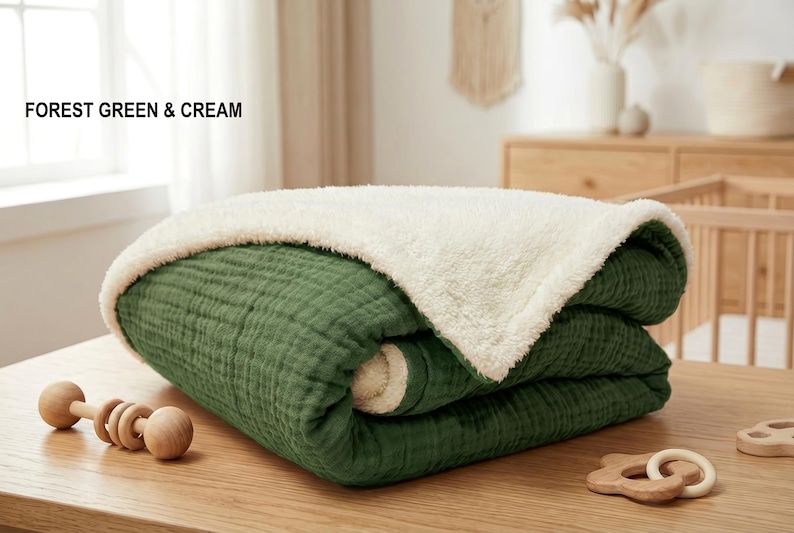 K&ouml;nnte beinhalten: Eine gefaltete Babydecke in Waldgr&uuml;n und Creme. Die Decke hat auf der gr&uuml;nen Seite ein strukturiertes, gestepptes Aussehen und eine weiche, pl&uuml;schige cremefarbene Seite. Der Text "FOREST GREEN & CREAM" befindet sich oben links.