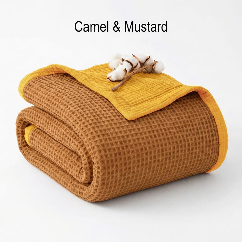 May include: A folded camel-colored waffle-weave blanket with a mustard yellow border and top layer. The blanket is topped with a sprig of cotton. The text "Camel & Mustard" is displayed at the top.