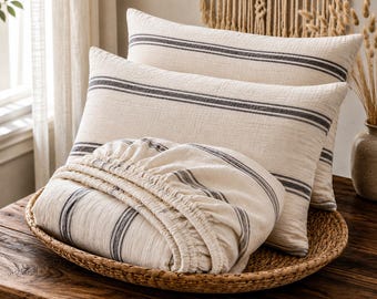 Op de afbeelding: Twee rechthoekige kussens en een hoeslaken met een ivoorkleurige basis en donkergrijze horizontale strepen. De stof heeft een zichtbare, getextureerde weving. De tekst IVORY & FRENCH STRIPE staat in het wit onderaan de afbeelding.