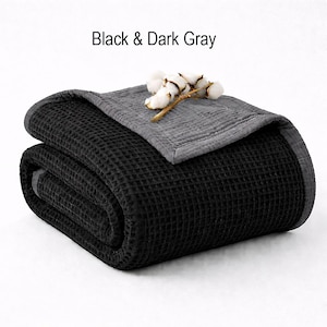 May include: Folded black waffle-weave blanket with a dark gray border and top layer. The text "Black & Dark Gray" is above the blanket. A sprig of cotton adds a decorative touch.