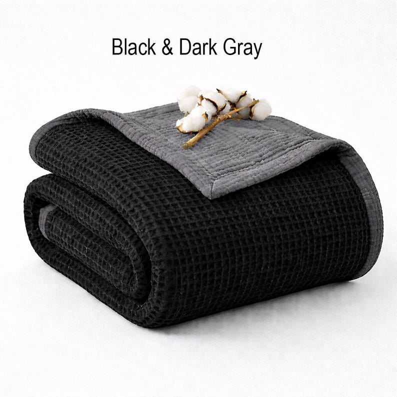 May include: Folded black waffle-weave blanket with a dark gray border and top layer. The text "Black & Dark Gray" is above the blanket. A sprig of cotton adds a decorative touch.