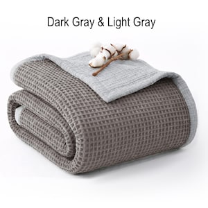 May include: A folded dark gray waffle-weave blanket with a light gray border and top layer. The blanket is adorned with a sprig of cotton. The text "Dark Gray & Light Gray" is displayed at the top.