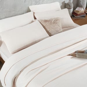 May include: A white waffle-textured bedding set with a fluffy faux fur throw pillow. The bedding is arranged on a bed with a wooden headboard.