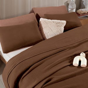 May include: A bedding set featuring a dark brown textured waffle-weave duvet cover and matching rectangular pillows. The arrangement includes two light brown pillows, a square cream-colored faux fur pillow, and a small white ceramic arch sculpture.