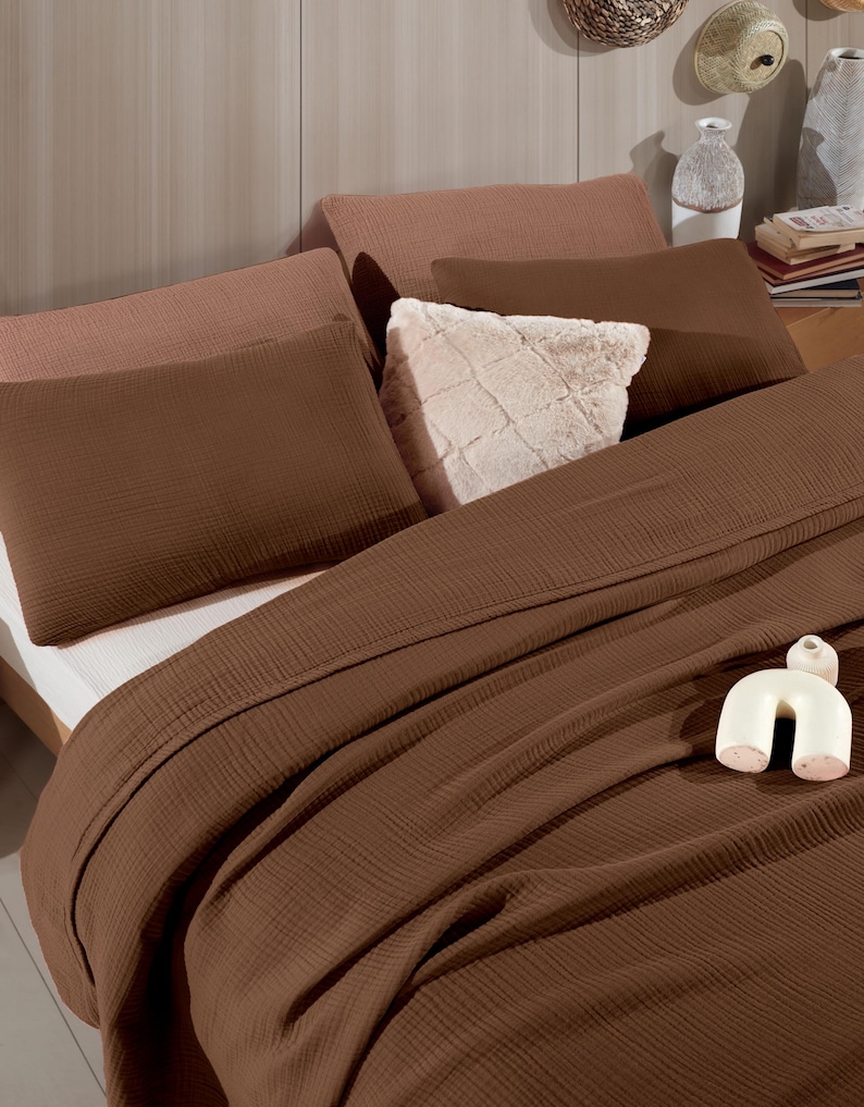 May include: A bedding set featuring a dark brown textured waffle-weave duvet cover and matching rectangular pillows. The arrangement includes two light brown pillows, a square cream-colored faux fur pillow, and a small white ceramic arch sculpture.