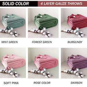 May include: Six folded gauze throws in different colours: mint green, forest green, burgundy, soft pink, rose colour, and damson. The throws are arranged in two rows of three, with a white cotton branch in front of each throw.
