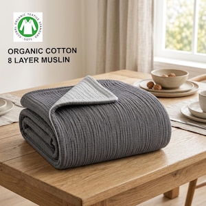 Könnte beinhalten: Eine gefaltete 8-lagige Musselindecke mit einer dunkel anthrazitfarbenen Außenseite und einer hellgrauen Innenseite. Das Textil ist als Bio-Baumwolle gekennzeichnet, mit dem Global Organic Textile Standard Logo und dem Text ORGANIC COTTON 8 LAYER MUSLIN.