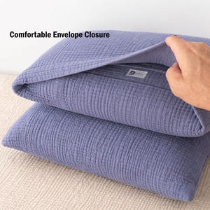 Pode incluir: Duas fronhas empilhadas, na cor azul-arroxeado, com um tecido texturizado e enrugado. A fronha superior est&aacute; parcialmente aberta, revelando o fecho envelope. O texto "Comfortable Envelope Closure" &eacute; vis&iacute;vel.