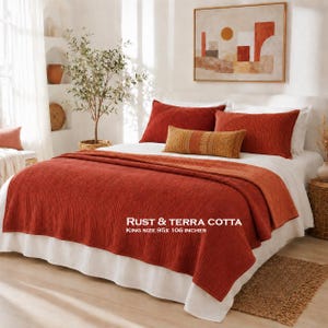 May include: A king size bedspread measuring 95x106 inches in a rust and terra cotta color. The bedding set includes two large rust-colored pillows and a smaller, rectangular, textured accent pillow in a golden-brown hue.