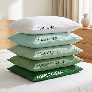 Pode incluir: Uma pilha de cinco almofadas quadradas em tons de verde e branco, com os textos "PURE WHITE", "AQUA GREEN", "SAGE GREEN", "EMERALD GREEN" e "FOREST GREEN" impressos em cada almofada. As almofadas est&atilde;o numa cama branca.