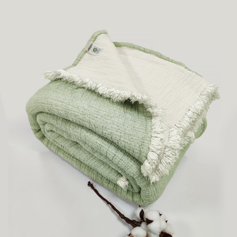 May include: A soft, green and white waffle weave throw blanket with a fringed edge. The blanket is folded and displayed on a white surface.
