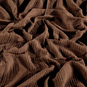May include: A solid dark brown fabric featuring a distinct crinkled, double gauze texture. The material is draped in deep folds and ripples, creating a pattern of light and shadow across the surface of the soft, lightweight textile.