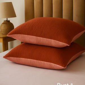Pode incluir: Duas almofadas cor de ferrugem com uma combina&ccedil;&atilde;o terracota, em uma cama. As almofadas t&ecirc;m uma superf&iacute;cie texturizada e uma borda p&ecirc;ssego contrastante. O texto "Rust & Terra-cotta combination" &eacute; vis&iacute;vel.