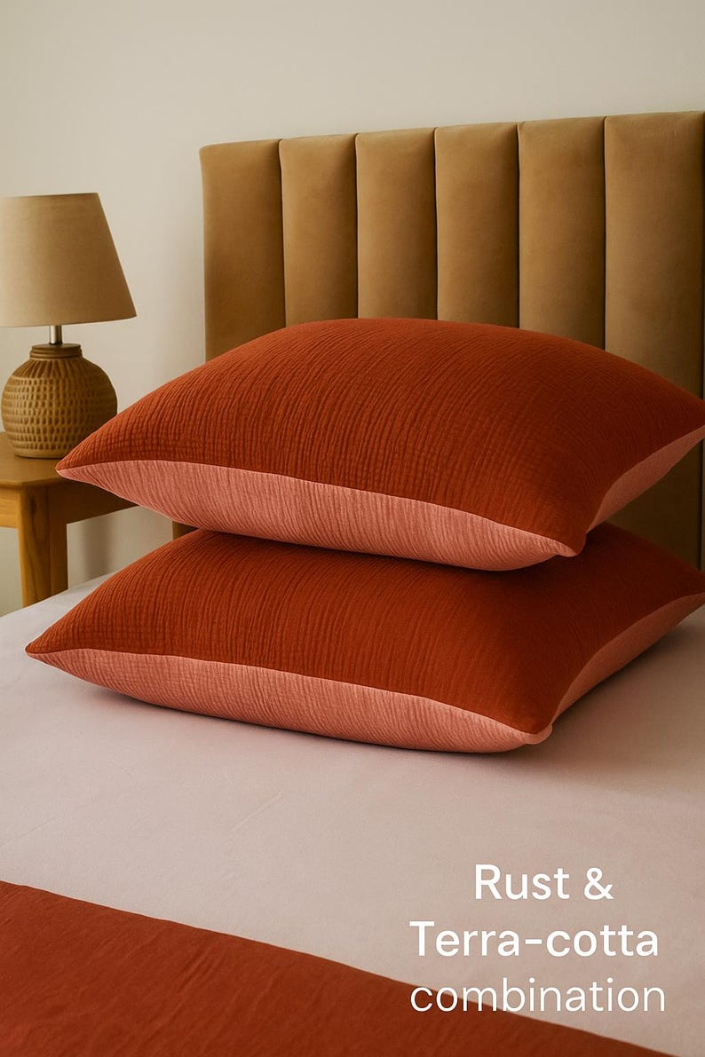Pode incluir: Duas almofadas cor de ferrugem com uma combina&ccedil;&atilde;o terracota, em uma cama. As almofadas t&ecirc;m uma superf&iacute;cie texturizada e uma borda p&ecirc;ssego contrastante. O texto "Rust & Terra-cotta combination" &eacute; vis&iacute;vel.