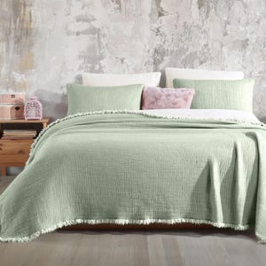 May include: A sage green throw blanket with a fringe border. The blanket is folded on a bed with white and sage green pillows.