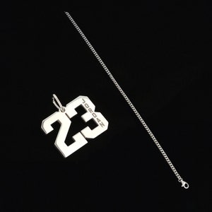 May include: Silver chain necklace with a silver pendant featuring the number 23 and the word "JORDAN" inscribed on it.