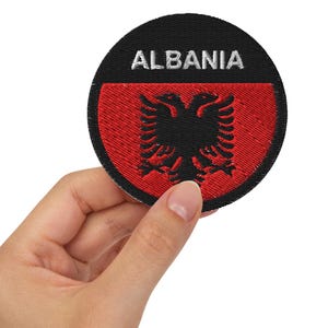 May include: A black and red embroidered patch with the Albanian flag and the word "ALBANIA" in white lettering.