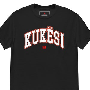 May include: Black t-shirt with a white "KUKËSI" text in an arch with a red outline. The Albanian flag is below the text.