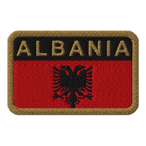 May include: A brown and gold embroidered patch with the word "ALBANIA" in gold letters and a black double-headed eagle on a red background.