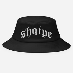 May include: Black bucket hat with white embroidered text that reads "shqipe".