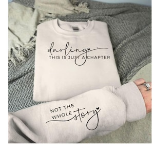May include: A white sweatshirt with the text "darling, this is just a chapter, not the whole story" in black cursive font with a small heart symbol after each sentence.
